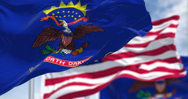 The North Dakota state flag waving along with the national flag of the United States of America. In the background there is a clear sky. North Dakota is a U.S. state in the Upper Midwest clipart