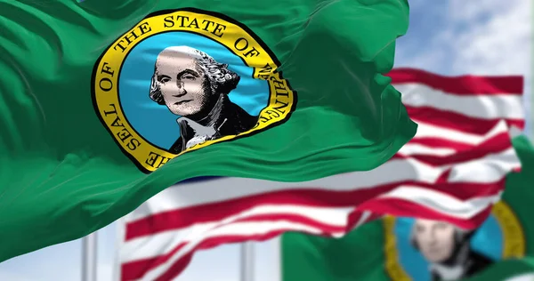 The Washington state flag waving along with the national flag of the United States of America. Washington is a state in the Pacific Northwest region of the Western United States