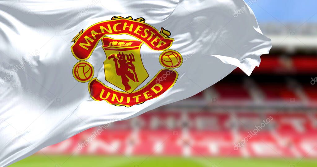 Manchester, UK, May 2022: The flag of Manchester United waving with Old Trafford stadium blurred in background.