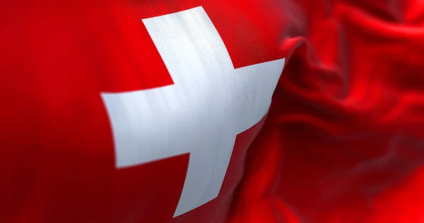 Close-up view of the swiss national flag waving in the wind. Switzerland is a landlocked country located in Europe. Fabric textured background. Selective focus
