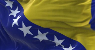 Close-up view of the Bosnia and Herzegovina national flag waving in the wind. Fabric textured background. Selective focus. Seamless loop in slow motion