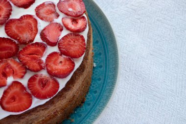 Çilekli kek ve mavi tabakta krema. Beyaz masa örtüsü üzerinde Yaz Çileği ve Kremalı Kek. Üst görünüm, boşluğu kopyala. Yaz ortası yemeği.