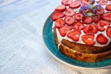 Çilekli kek ve mavi tabakta krema. Beyaz masa örtüsü üzerinde Yaz Çileği ve Kremalı Kek. Üst görünüm, boşluğu kopyala. Yaz ortası yemeği.