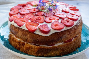 Çilekli kek ve mavi tabakta krema. Beyaz masa örtüsü üzerinde Yaz Çileği ve Kremalı Kek. Üst görünüm, boşluğu kopyala. Yaz ortası yemeği.