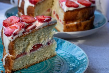 Çilekli kek ve mavi tabakta krem şanti. Beyaz masa örtüsü üzerinde Yaz Çileği ve Kremalı Kek. Üst görünüm, boşluğu kopyala. Yaz ortası yemeği.