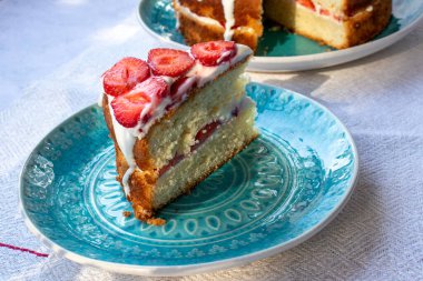 Çilekli kek ve mavi tabakta krem şanti. Beyaz masa örtüsü üzerinde Yaz Çileği ve Kremalı Kek. Üst görünüm, boşluğu kopyala. Yaz ortası yemeği.