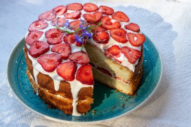 Çilekli kek ve mavi tabakta krema. Beyaz masa örtüsü üzerinde Yaz Çileği ve Kremalı Kek. Üst görünüm, boşluğu kopyala. Yaz ortası yemeği.