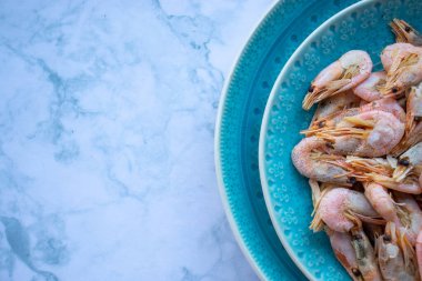 Maydanozlu ve limonlu karides, beyaz mermer masa arka planında mavi bir seramik kasede. Sağlıklı Akdeniz ürünleri. Üst görünüm, düz görünüm, kopyalama alanı