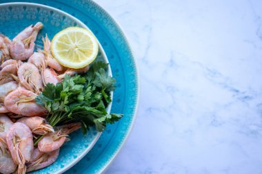 Maydanozlu ve limonlu karides, beyaz mermer masa arka planında mavi bir seramik kasede. Sağlıklı Akdeniz ürünleri. Üst görünüm, düz görünüm, kopyalama alanı