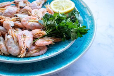 Maydanozlu ve limonlu karides, beyaz mermer masa arka planında mavi bir seramik kasede. Sağlıklı Akdeniz ürünleri. Üst görünüm, düz görünüm, kopyalama alanı