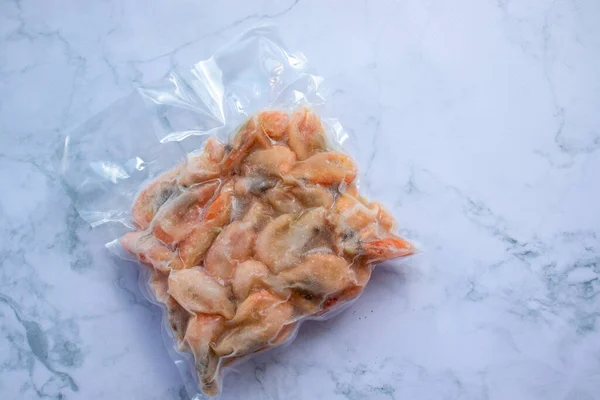 Frozen shrimps in vacuum transparent plastic packaging bag on white table background. Top view, copy space, flat lay