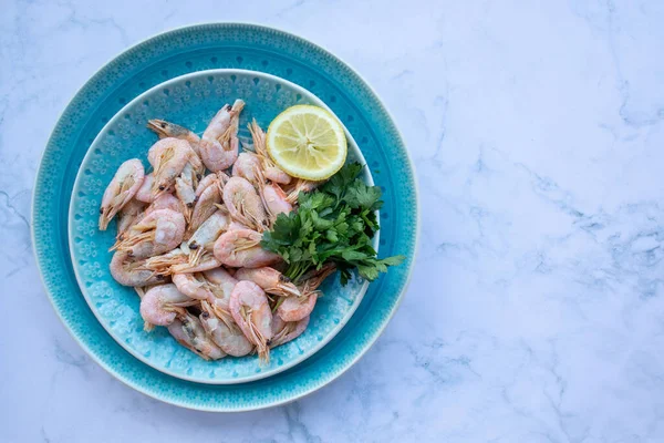 ooked shrimp with parsley and lemon in a blue ceramic bowl on a white marble table background. Healthy Mediterranean seafood. Top view, flat lay, copy space