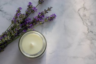 Lavanta çiçekleri ve beyaz mermer masa arkaplanındaki kavanozda aromatik beyaz mum. Rahatlatıcı spa konsepti. Üst görünüm, düz görünüm, kopyalama alanı