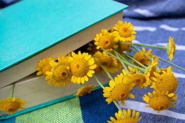 Açık havada kumaş arka planda kitap ve sarı çiçekler. Doğada dinlenmek, yaz tatili, roman okumaktan zevk almak..