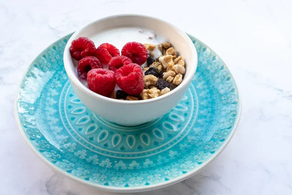 Bowl of homemade granola cereal with greek yogurt and fresh raspberry berries on white marble table background. Top view, flat lay, copy space. Healthy eating concept.