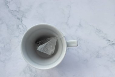 Beyaz mermer masa arka planında çay poşeti. Üst görünüm, boşluğu kopyala. Boş bardakta çay poşeti. Çay saati konsepti