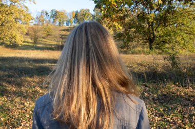 Sonbahar parkında uzun sarı saçlı bir kadının portresi. Arka plan