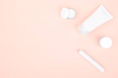Pembe arka planda beyaz makyaj malzemeleri, el kremi, yüz kremi ve ruj.