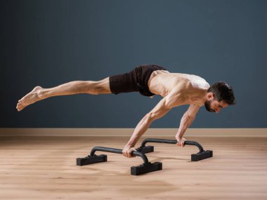 A calisthenics instructor trains alone at home for a perfect straddle planche with Push up Bars clipart