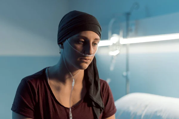 Young sad woman with cancer sitting on the hospital bed, she is looking at camera, illness and healthcare concept