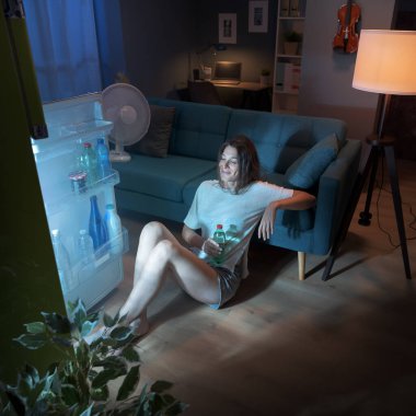 Kadın sıcaktan acı çekiyor ve buzdolabının önünde serinliyor.