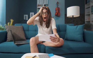 Şok olmuş bir kadın pahalı faturalarını kontrol ediyor.