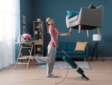 Verimli mutlu ev hanımı dairesini temizliyor: tek eliyle koltuğu kaldırıyor ve yerleri süpürüyor, zahmetsiz ev idaresi konsepti