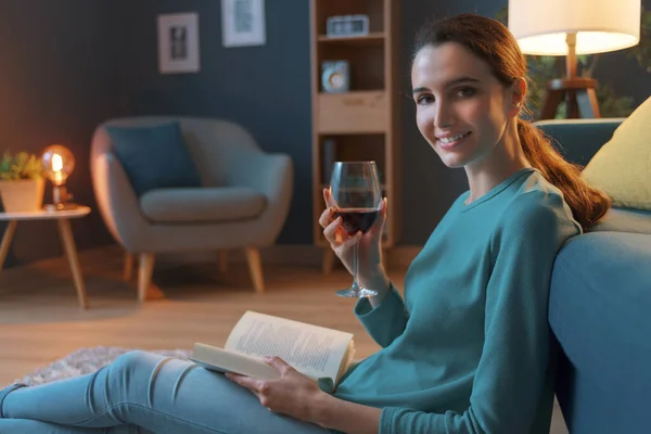 自宅でリラックスしている若い女性 彼女はリビングルームの床に座って ワインを飲み 本を読んでいます — ストック写真