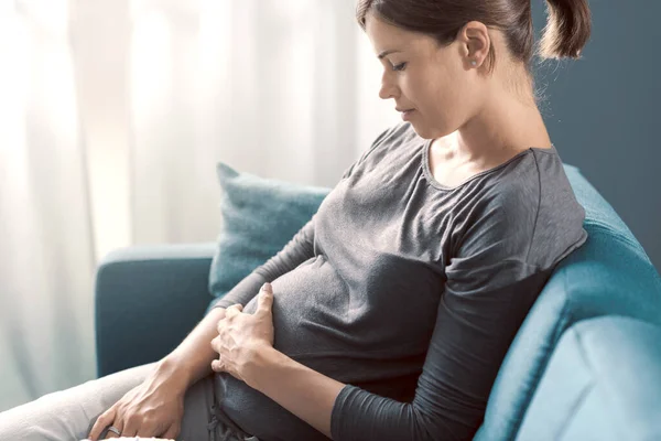 Νεαρή Έγκυος Γυναίκα Κάθεται Στον Καναπέ Στο Σπίτι Και Χαλαρώνει — Φωτογραφία Αρχείου