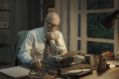 Profesyonel iş adamı ve gazeteci ofis masasında oturuyor ve çalışıyor. Daktiloyla düşünüyor ve daktilo yazıyor.