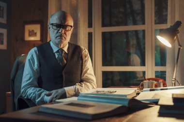 Kendine güvenen akademisyen masada oturuyor ve poz veriyor. Kitap okuyor.