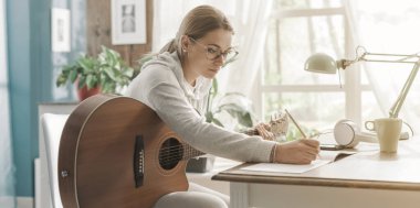 Evde gitar çalan ve müzik besteleyen genç yaratıcı kadın.