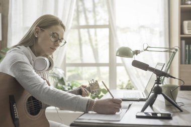 Gitar çalan ve müziğini kaydeden bir kadın, dizüstü bilgisayarını ve mikrofonunu kullanıyor.
