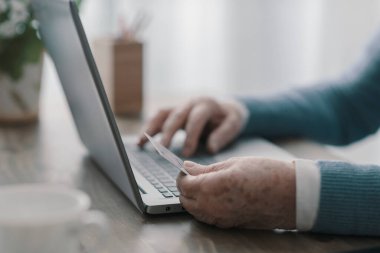 Üst düzey bir kadın internetten kredi kartı kullanıyor ve dizüstü bilgisayarında yazı yazıyor.