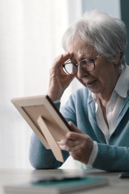 Evdeki üzgün kadın kocasının yasını tutuyor, elinde bir resim tutuyor ve ağlıyor.