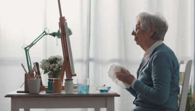 Son sınıftaki mutlu kadın resmine bakıyor, ellerini bir bezle temizliyor.