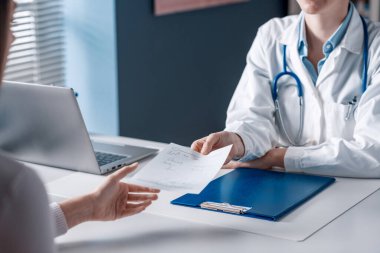 Doktor masada oturuyor ve bir hastaya reçete yazıyor.
