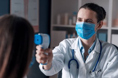 Doktor, bir hastanın vücut ısısını kızılötesi termometre, koronavirüs önleme kavramı kullanarak ölçüyor.
