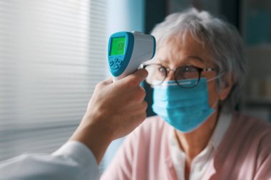Doktor, temassız kızılötesi termometre kullanarak kıdemli bir hastanın vücut ısısını ölçüyor.