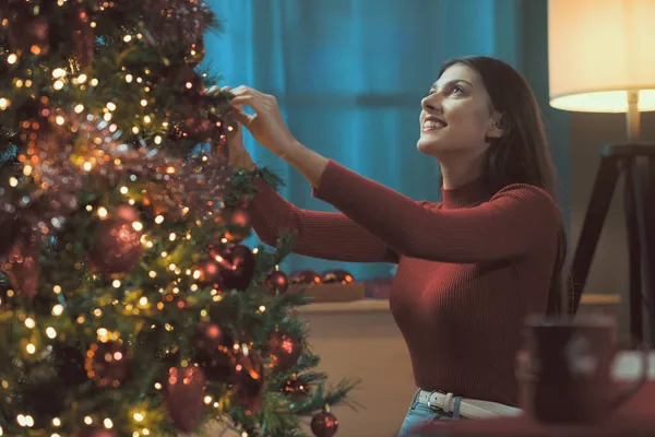 漂亮的女人在家里装饰着圣诞树 她挂着装饰品和浴盆 还有节日和庆祝的念头 — 图库照片
