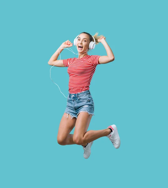 ヘッドフォンをして音楽を聴いている陽気な若い女性 彼女はジャンプして興奮しています — ストック写真