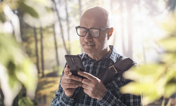 森の中を歩く幸せな中年の男と彼のスマートフォンを使用して — ストック写真
