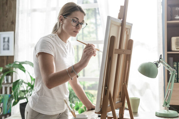 Young confident woman painting on canvas in her studio, creativity and hobby concept