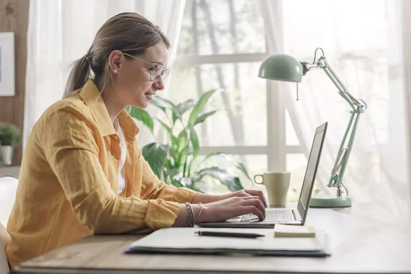 若いビジネスマンの女性が机に座って家から仕事をしてる彼女はノートパソコンと接続してる — ストック写真
