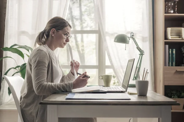 若いビジネスマンの女性が机に座って家から仕事をしてる彼女はノートパソコンと接続してる — ストック写真
