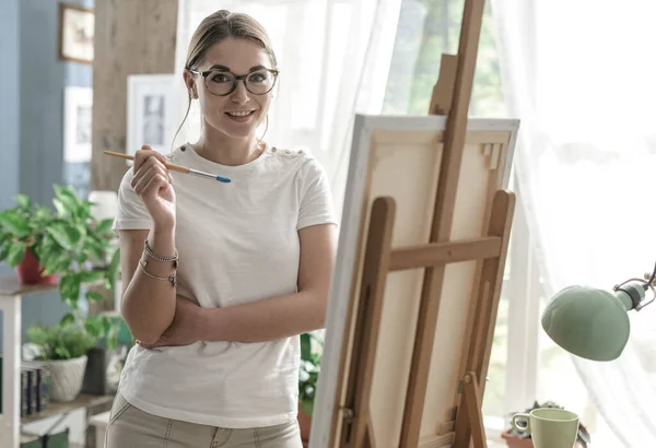 彼女のスタジオでキャンバス上の若い笑顔の女性の絵 創造性と趣味のコンセプト — ストック写真