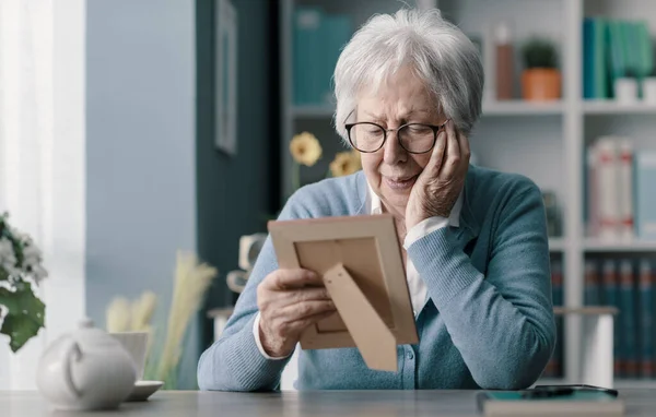 Sad senior woman mourning the loss of her husband, she is holding a picture and crying