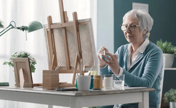幸せな先輩女性座って机の上に家と絵でキャンバス — ストック写真