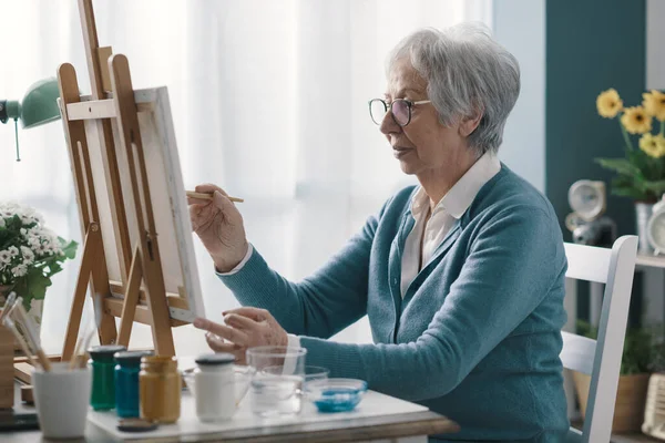 幸せな先輩女性座って机の上に家と絵でキャンバス — ストック写真