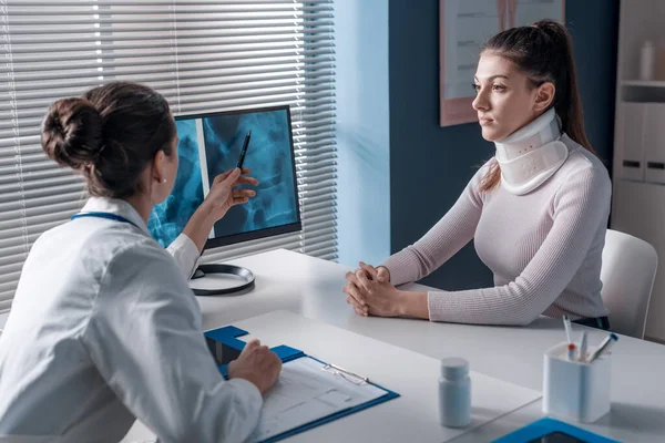 患者にX線を説明し コンピュータ画面を指している医師は 女性が子宮頸部の襟を着ている — ストック写真